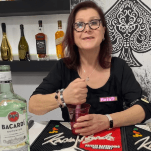 Bartender making a drink and smiling wearing black tshirt.